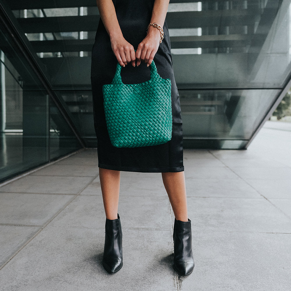 A model holding a small woven vegan leather tote bag against stairs.