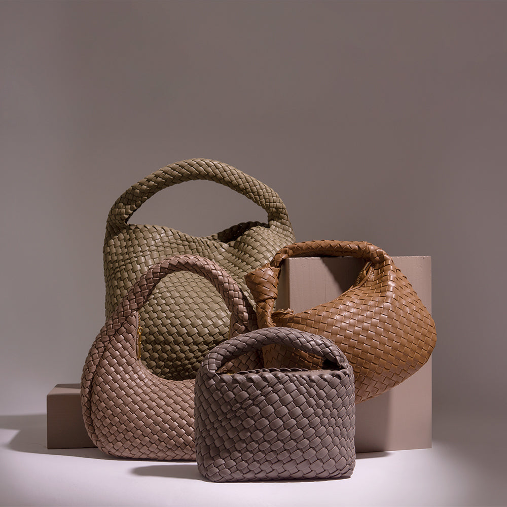 A still image of four woven vegan leather handbags against a brown wall.