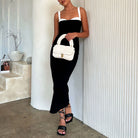 A model holding an ivory knitted crossbody handbag against a white wall.