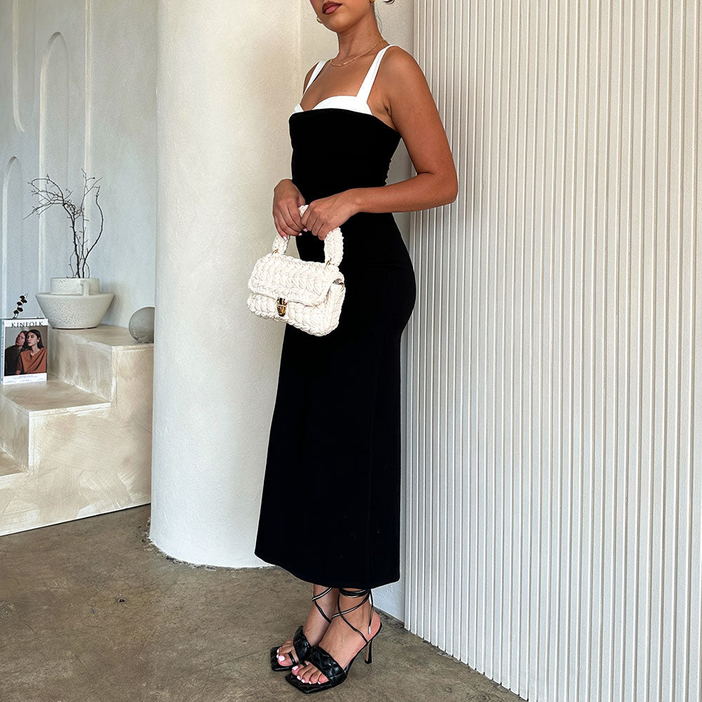 A model holding a white knitted handbag against a white wall. 
