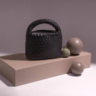 A still image of a small hand woven vegan leather top handle bag against a wooden prop.