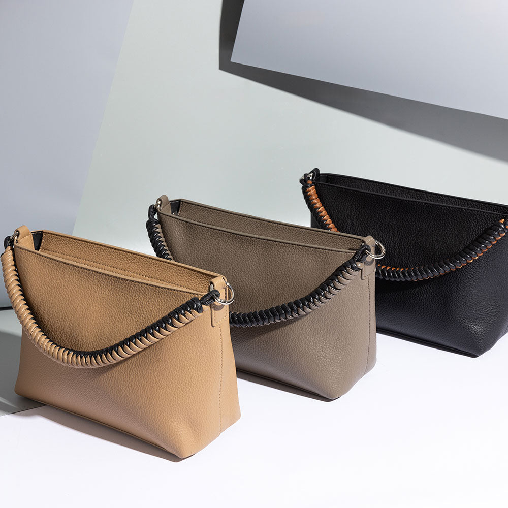 A still image of three small recycled vegan leather crossbody handbags with woven handles against a grey background. 