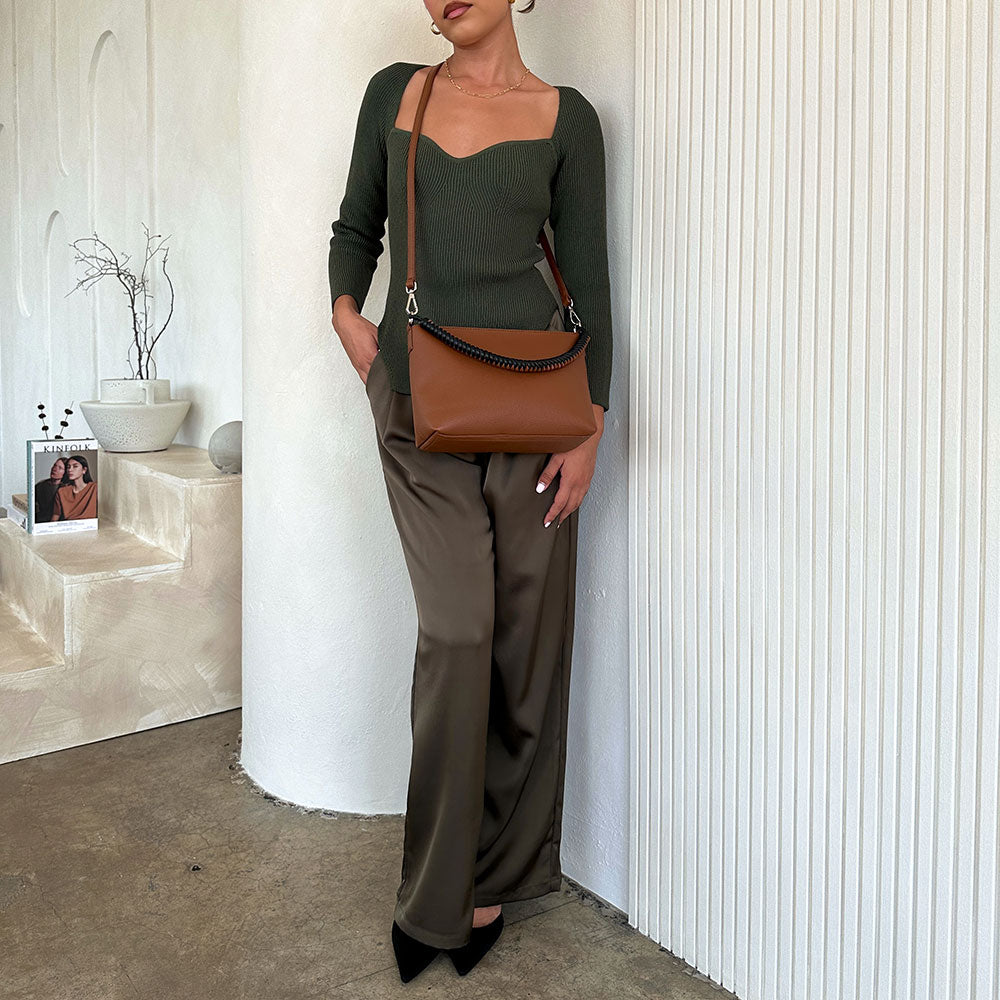 A model wearing a saddle small vegan leather crossbody handbag against a white wall. 