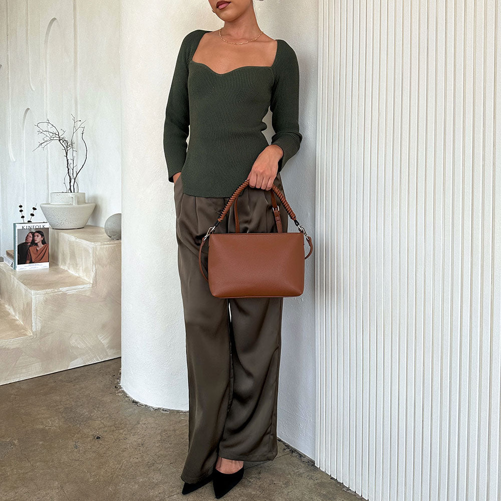 A model wearing a saddle vegan leather crossbody handbag against a white wall. 