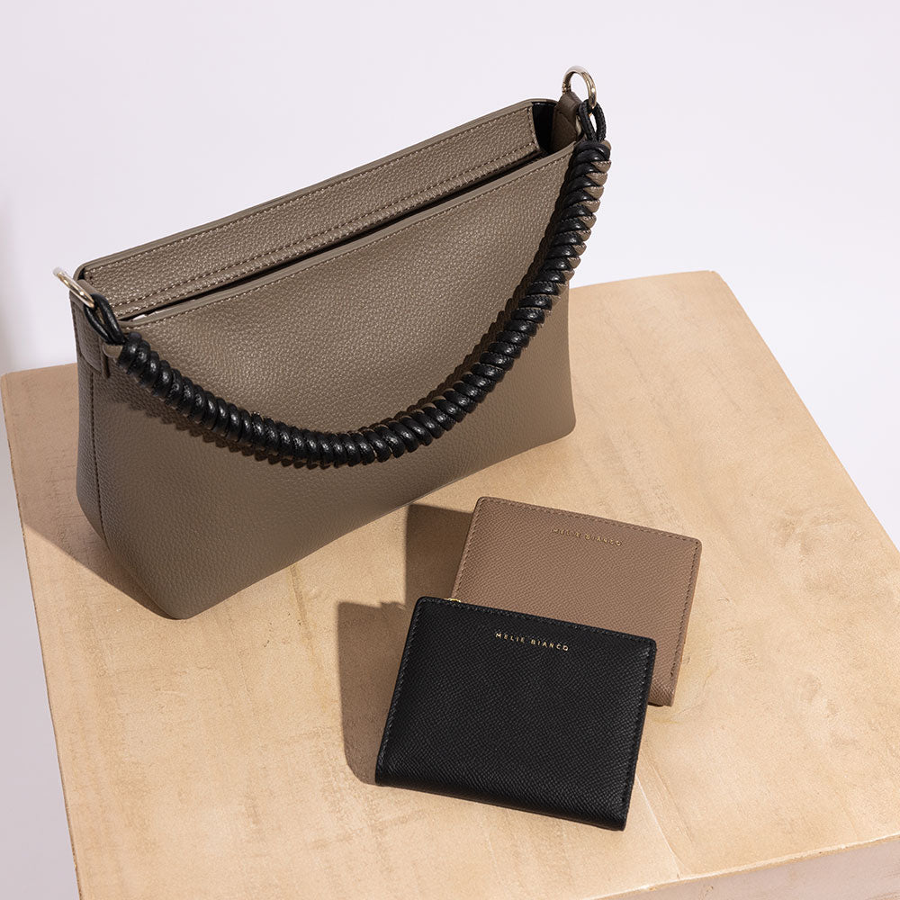 A still image of a small recycled vegan leather handbag with two wallets laying on a prop. 