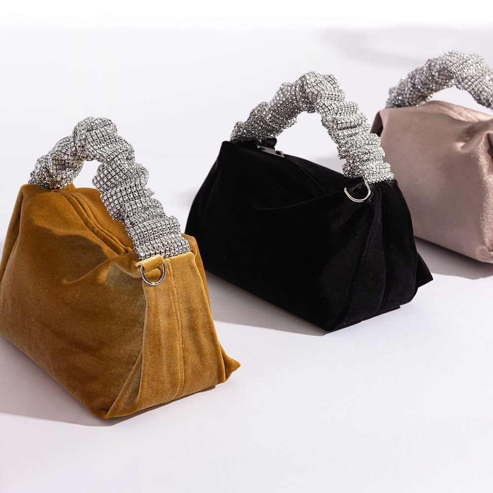 A still image of three velvet top handle bags with silver encrusted handle against a white wall. 