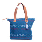 Front of the Angela Handwoven Tote in Lake Ripple pattern. It has horizontal zigzag stripes in red, light blue, and blue over a blue background. It has a blue tassel and leather handles.