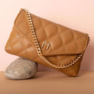 A still image of a camel quilted vegan leather shoulder bag against a rock. 