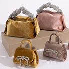 A still image of two medium velvet top handle bags and two mini velvet crossbody bags against a white wall. 