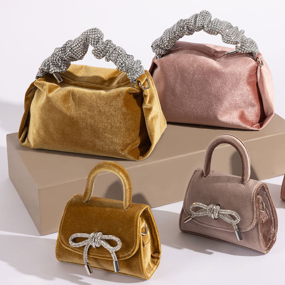 A still image of four different velvet handbags with silver encrusted bows and handles against a wooden prop.