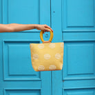 A model holds the hand woven artisan Dalila Midi Tote in Sunset Yellow over a blue painted door.