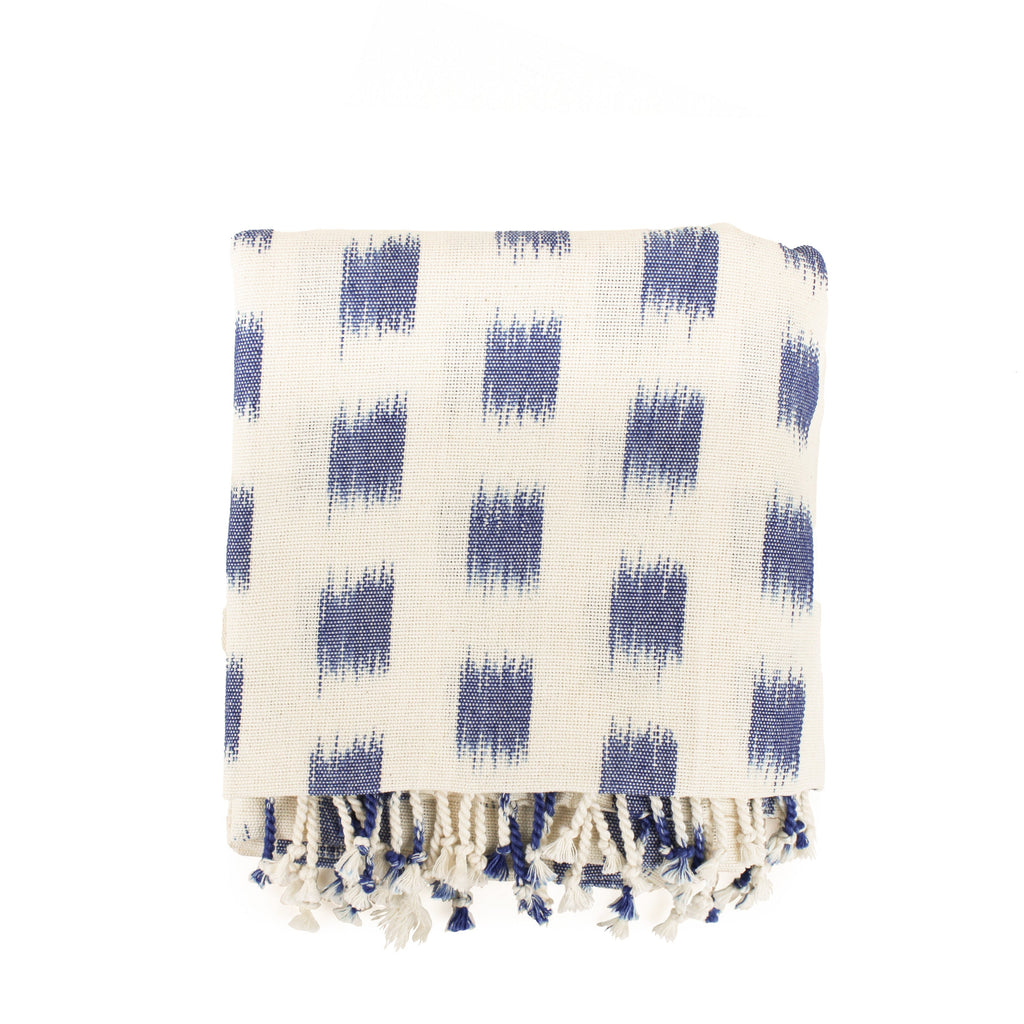Hand woven artisan Bartola Beach Blanket in Brushstrokes pattern. The blanket is folded, showing flame stitched blue squares and fringe on the edges.