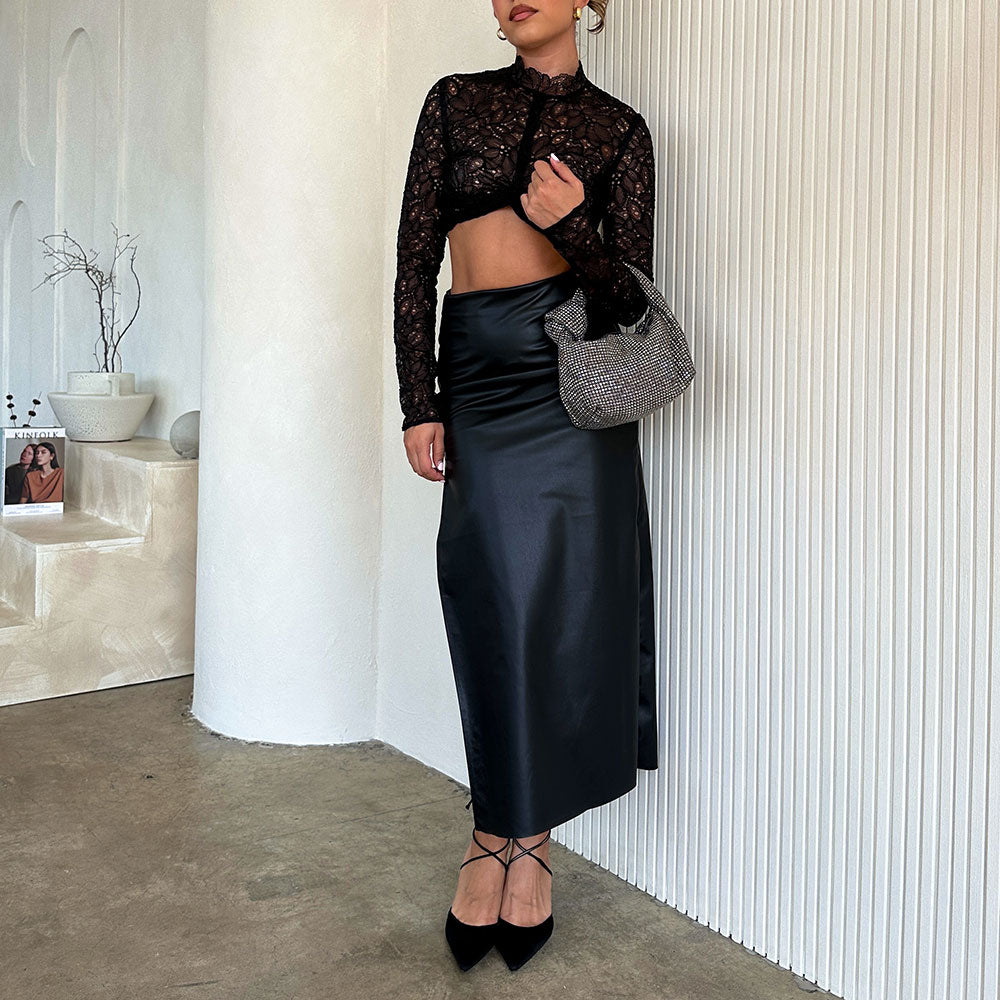 A model wearing a small crystal encrusted top handle bag against a white wall. 