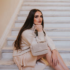 A model wearing a small crocheted vegan leather shoulder bag sitting on stairs. 