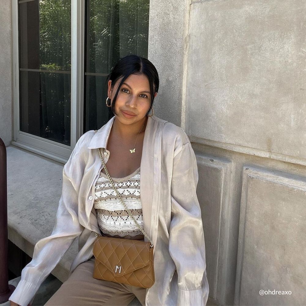 A model wearing a small camel quilted vegan leather shoulder bag against a wall outside. 