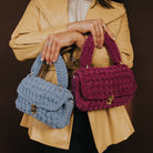 A model holding a sky knitted handbag and a plum knitted handbag crossed over each other. 