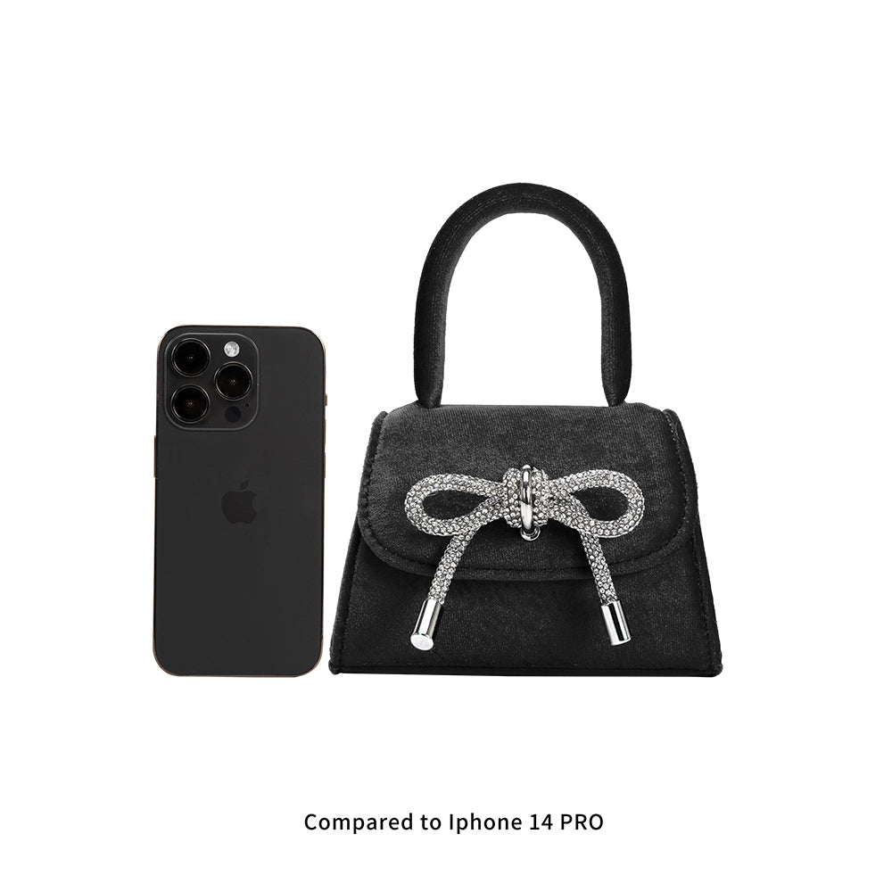 An iphone 14 pro size comparison image for a mini velvet top handle bag with an encrusted bow.