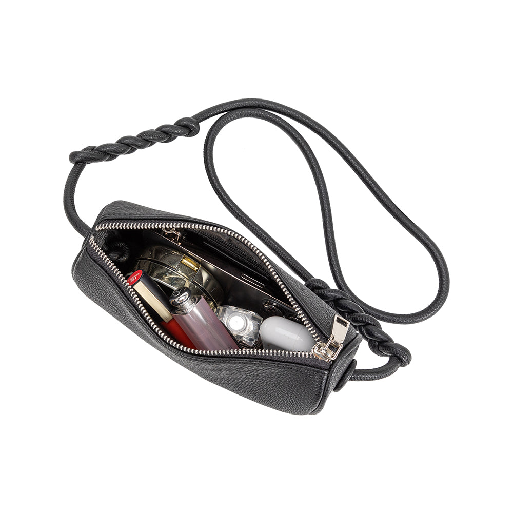 An inside view image of a small crescent shaped vegan leather crossbody bag with a phone, makeup, and earbuds. 