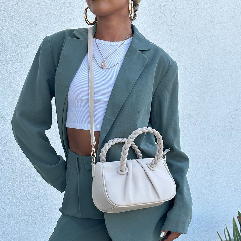 A model wearing a small recycled vegan leather crossbody bag against a white wall. 