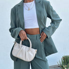 A model holding a small recycled vegan leather crossbody bag against a white wall. 