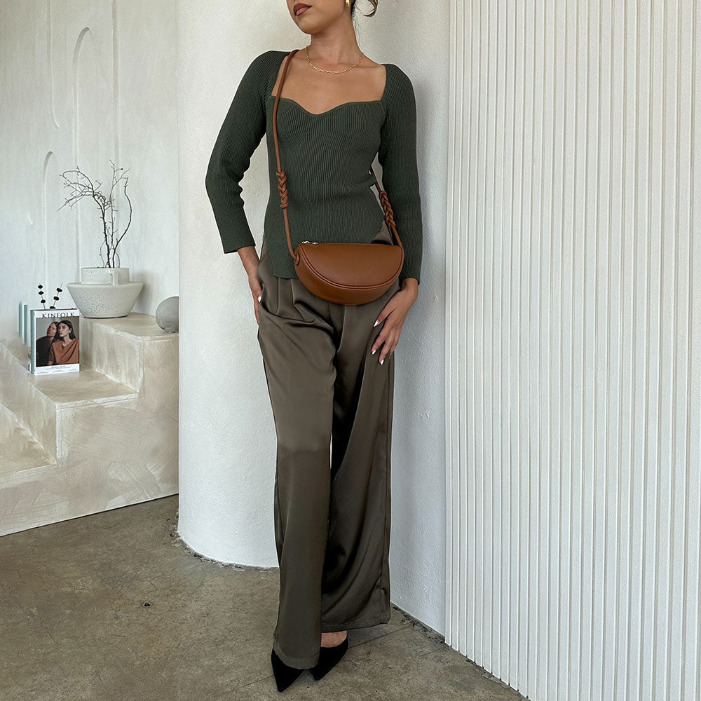 A model wearing a small crescent shaped vegan leather crossbody bag against a white wall. 