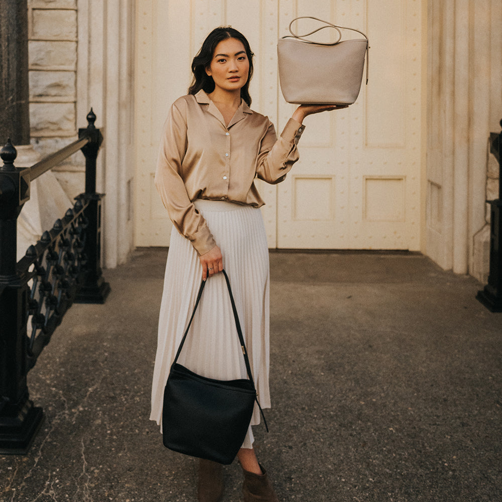 A model holding two recycled vegan leather shoulder bags outside a building. 