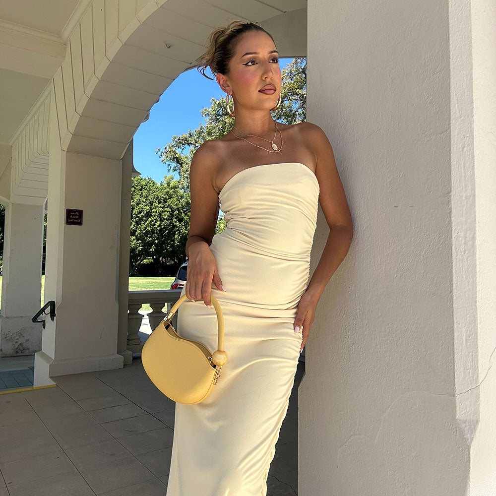 A model wearing a small yellow structured vegan leather crossbody bag with a marble pearl against a concrete wall.