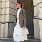 A model wearing a small woven vegan leather crossbody bag outside on stairs. 