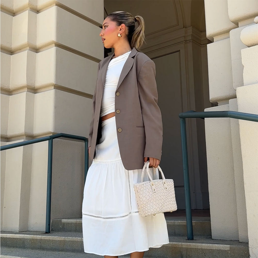 A model wearing a small woven vegan leather crossbody bag with a wrapped handle standing on stairs. 