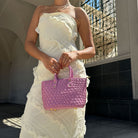 A model wearing a pink woven vegan leather crossbody bag against a black and white wall. 