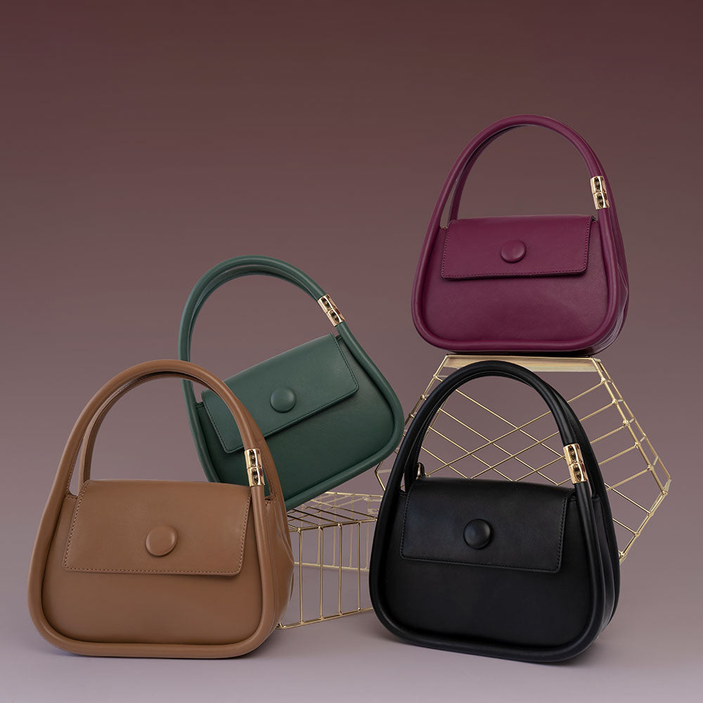 A still image of four structured vegan leather crossbody bags with double handles against a purple wall on top of gold props. 