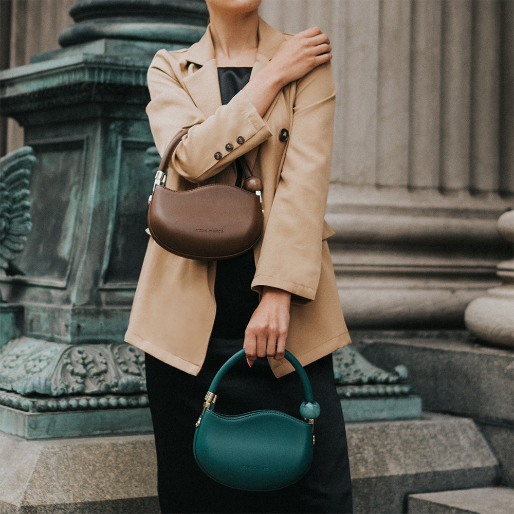 A model wearing two small structured vegan leather crossbody bag with a marble pearl accessory against a concrete background. 